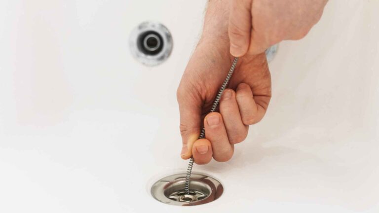 A hand performing drain maintenance using a snake to unclog a bathroom sink.
