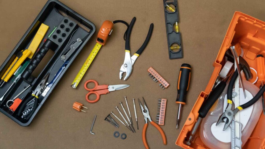 Various tools including screwdrivers, pliers, a tape measure, scissors, and a sump pump neatly arranged on a brown background.
