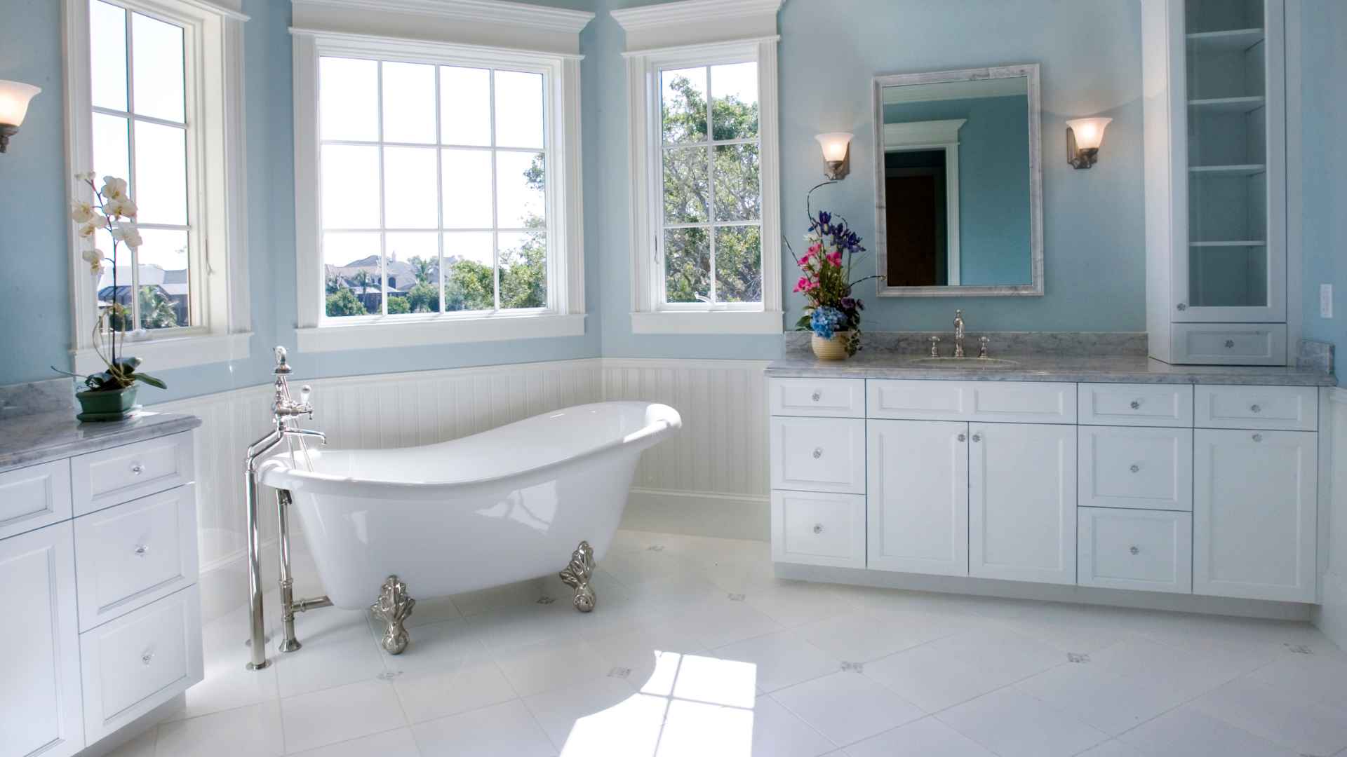 Spacious bathroom with a tub replacement, white cabinets, marble countertops, and large windows providing natural light.