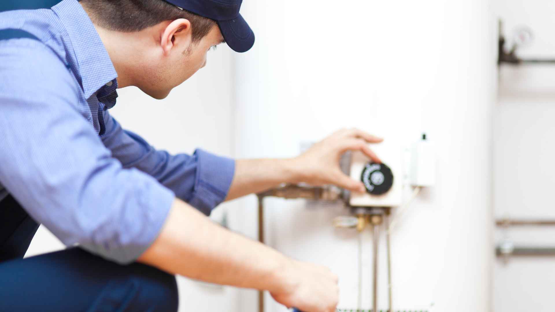 A technician adjusting the thermostat on a residential water heater system.