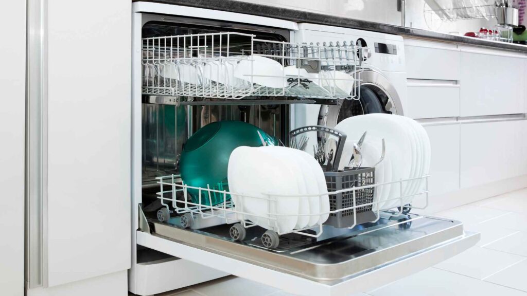 Open dishwasher with clean dishes including plates, bowls, and utensils, connected to kitchen plumbing in a modern setting.
