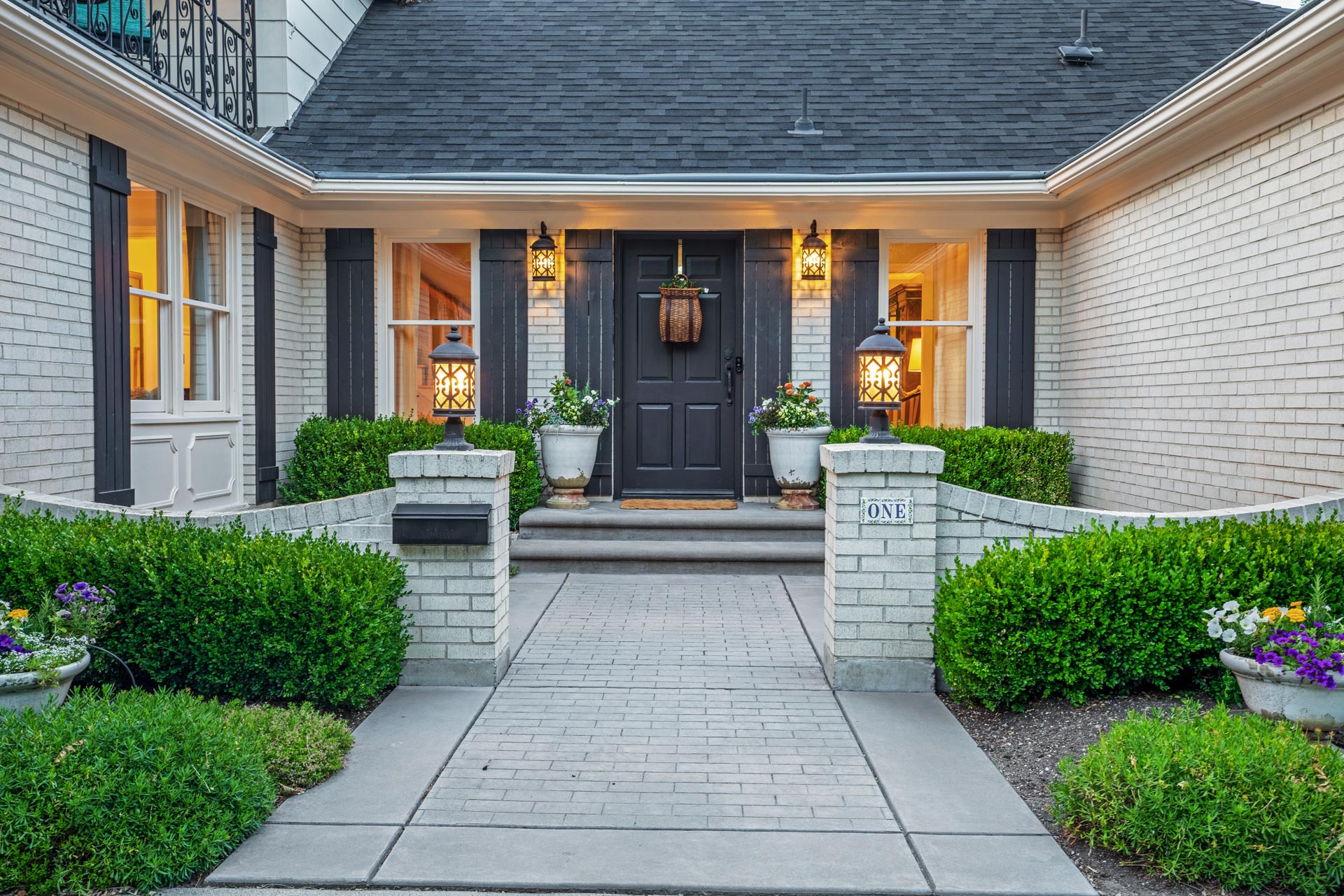 An inviting house entrance with a black door, symmetrical porch lights, and well-manicured landscaping featuring aspen maintenance.
