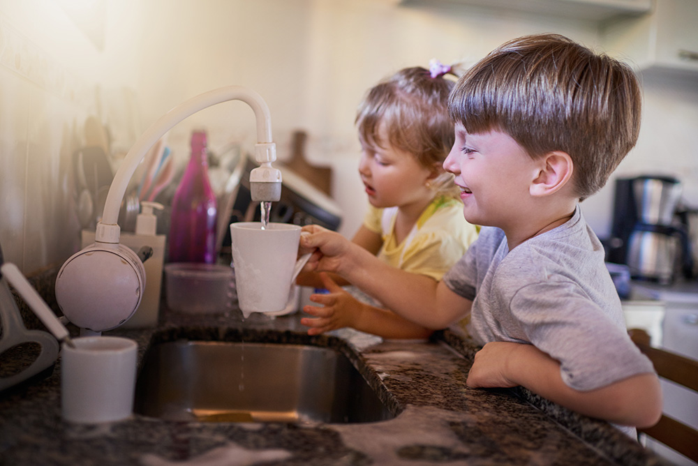 Two young children washing dishes at a Jackson kitchen sink.