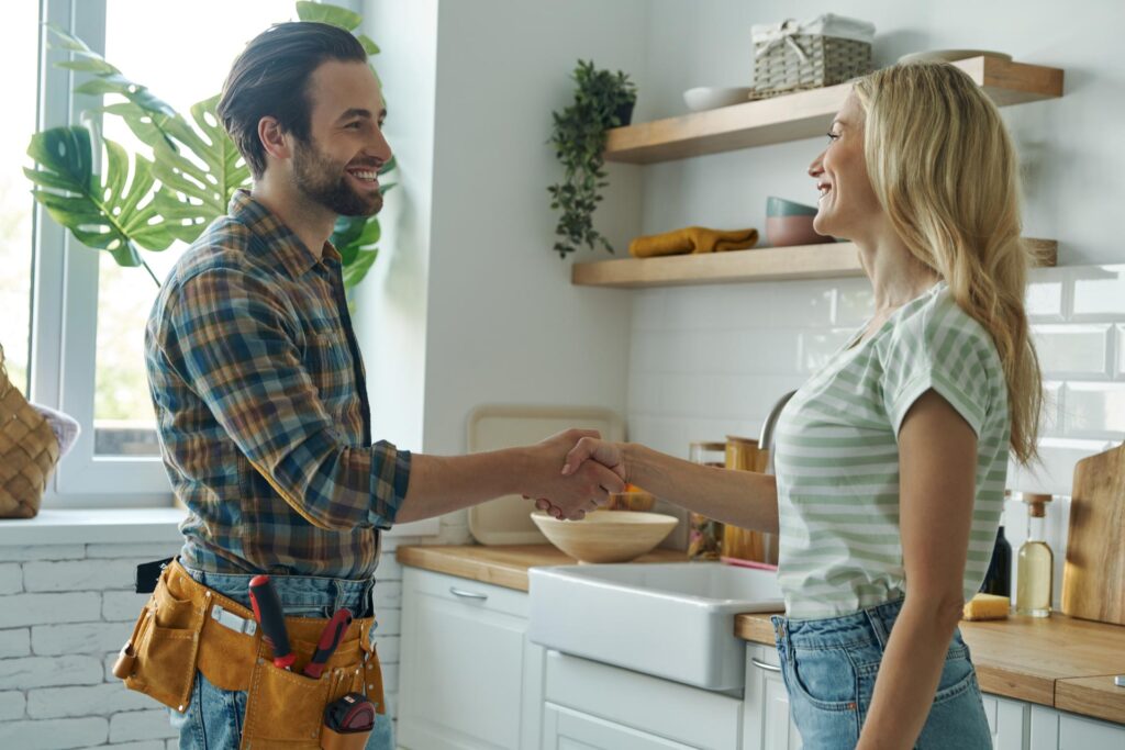 A smiling woman shaking hands with a handyman from Aspen Maintenance in a home kitchen.