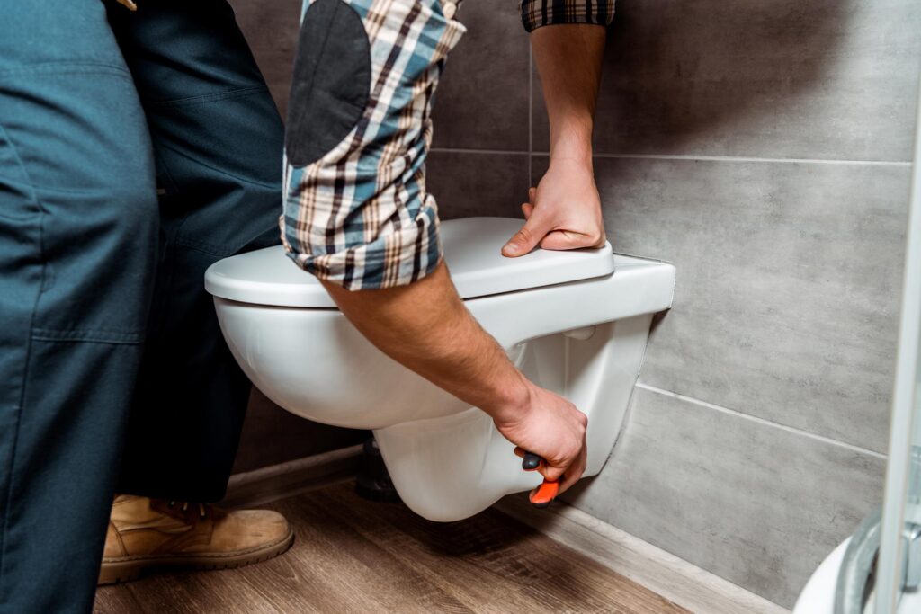 Two people performing Aspen maintenance or repairing a white toilet in a bathroom.