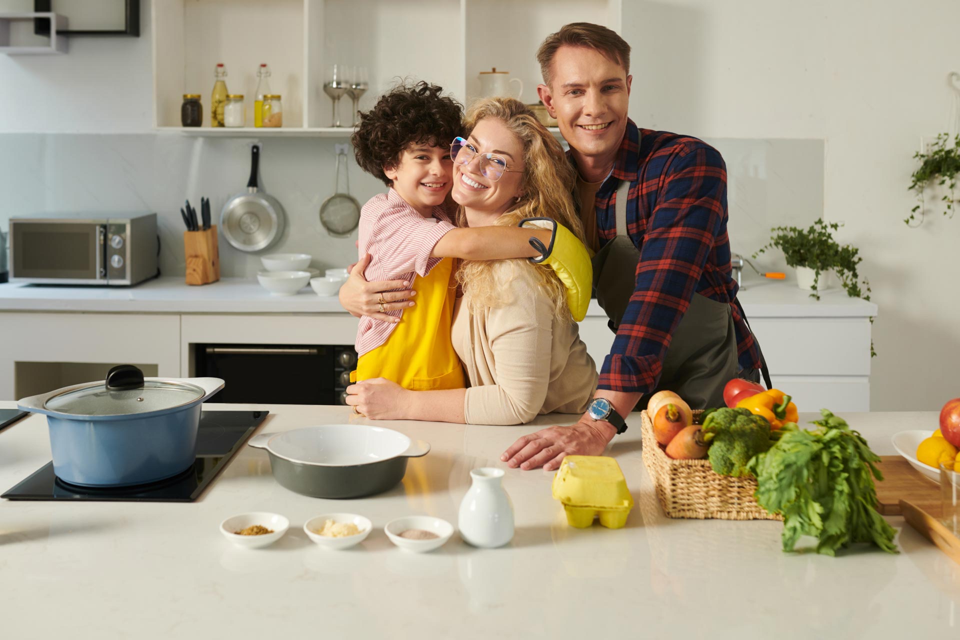 A happy family embracing in a home kitchen filled with fresh ingredients and cooking utensils, where the latest plumbing and water services ensure a seamless cooking experience.