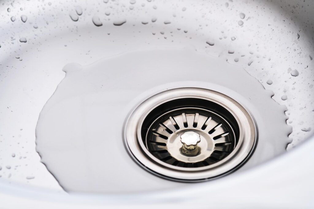 Close-up of water droplets in a clean, white sink with a visible Jackson Plumbing drain.