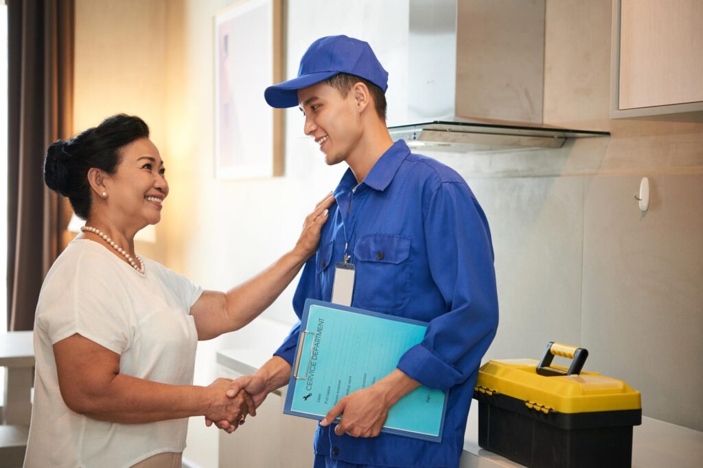 A smiling woman shaking hands with a technician in a blue uniform holding a clipboard, expressing gratitude for his home maintenance service in Aspen.