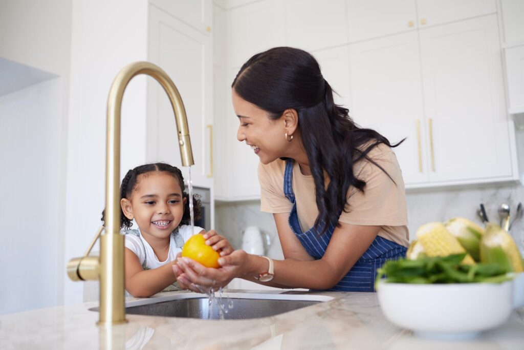 Mother and daughter washing fruit together in the kitchen, using Jackson water services.