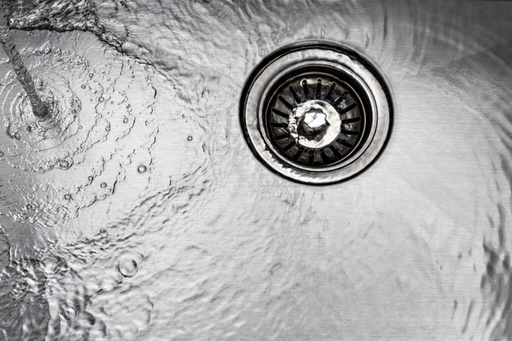 Water from home plumbing services swirling down a stainless steel kitchen sink drain.