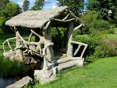 Rustic wooden gazebo with a thatched roof, situated by a small pond in a lush green park.