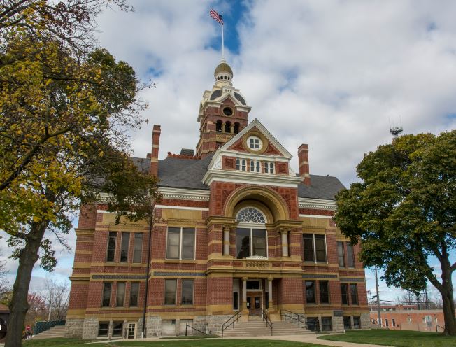 Historic county courthouse with a brick facade and a central clock tower displaying the american flag against a cloudy sky.