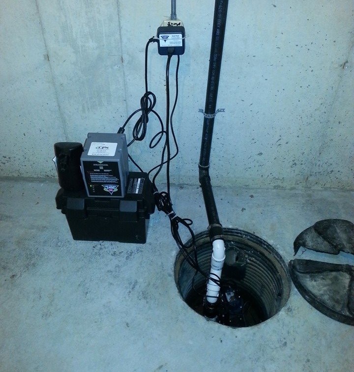 Sump pump system installed in a basement with a backup battery and discharge piping.