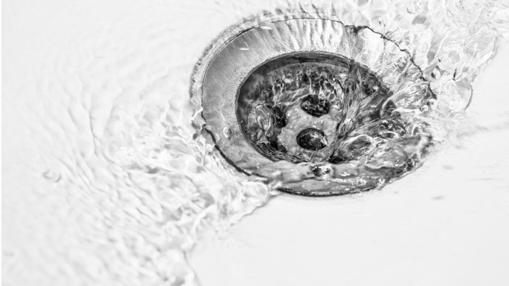 Water flows around and down a metal sink drain
