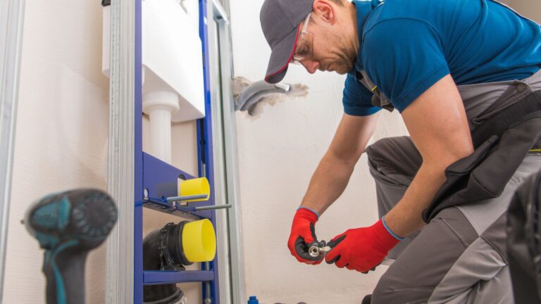 A plumber wearing red gloves and a blue cap installs or repairs in the bathroom