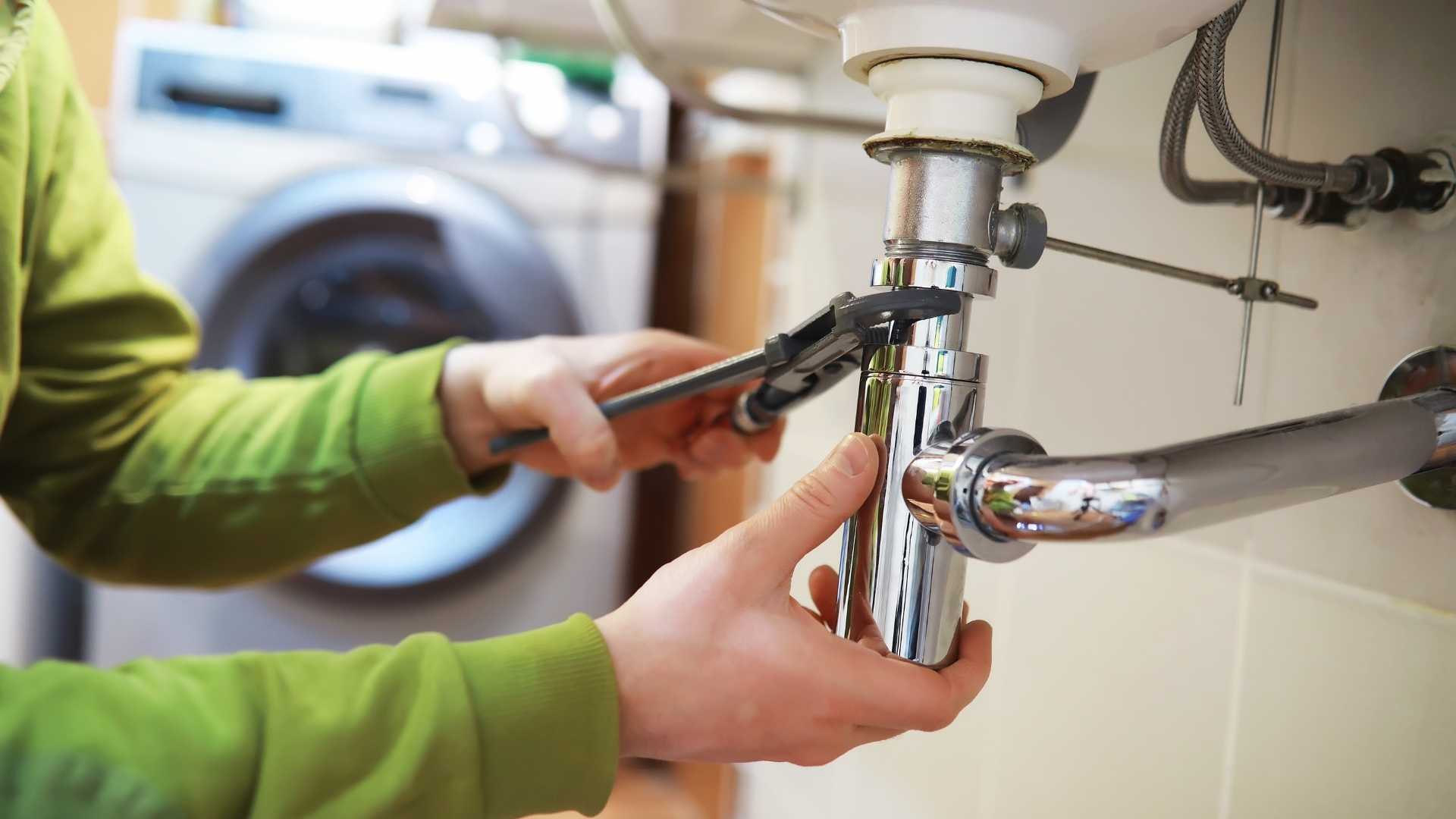 Person in a green shirt using a wrench to fix a pipe under a sink