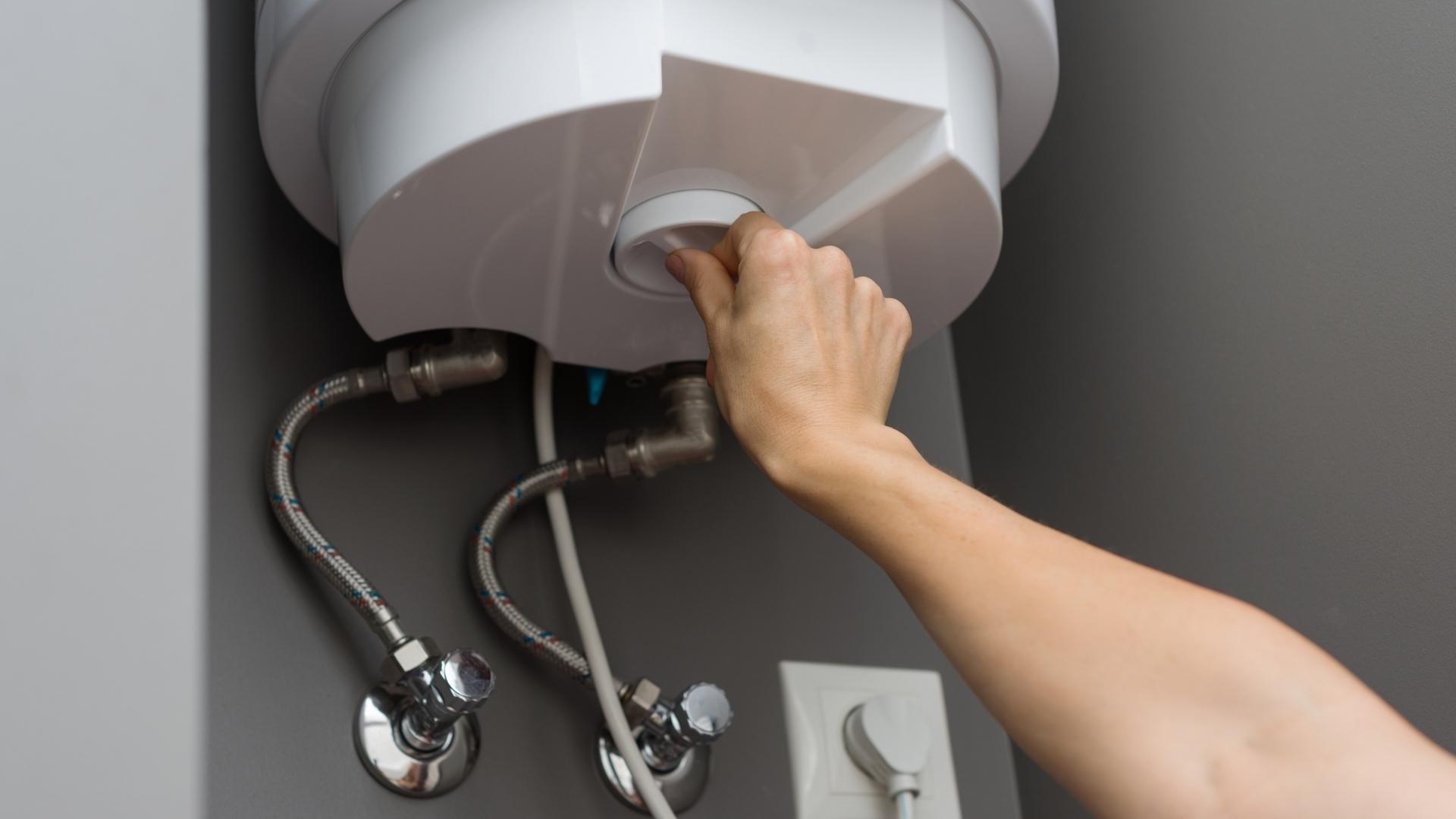 A person adjusts the knob on an electric water heater