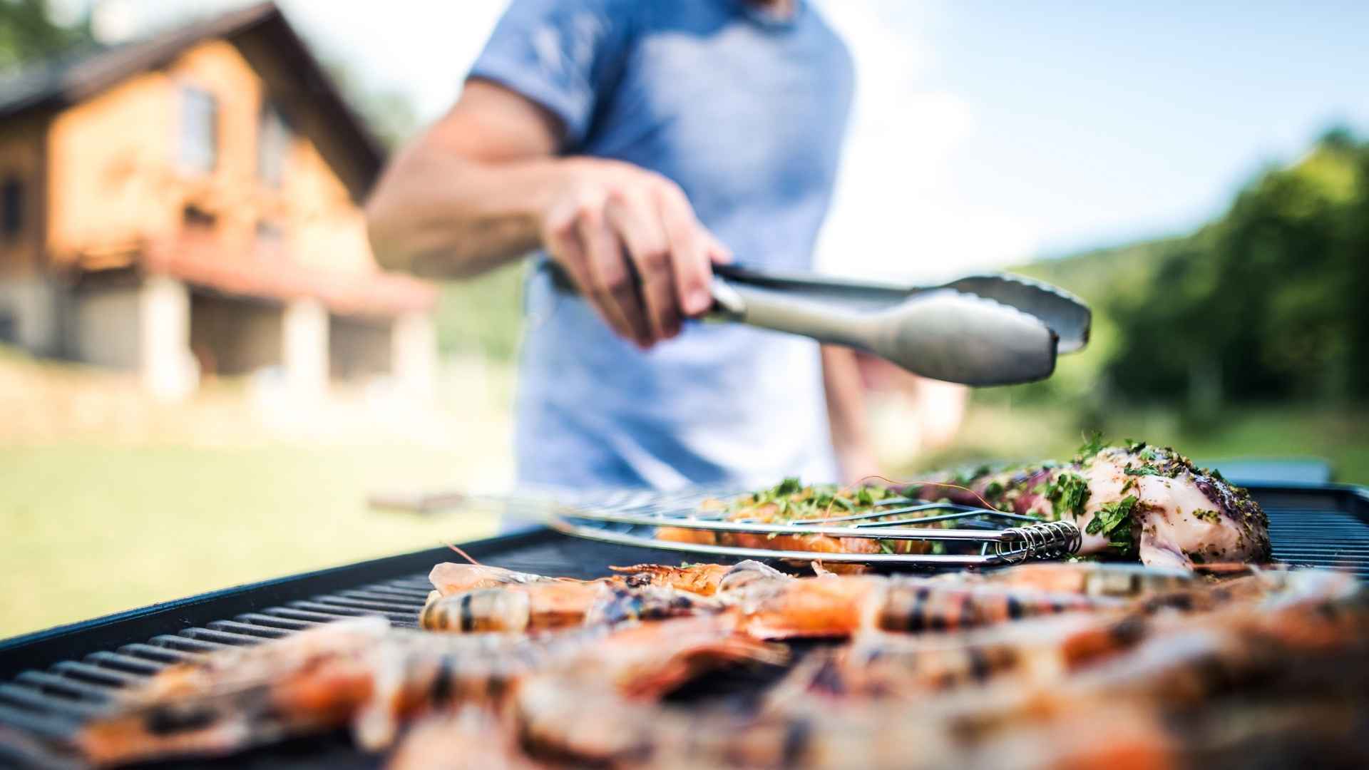 Person grilling shrimp and meat on an outdoor barbecue