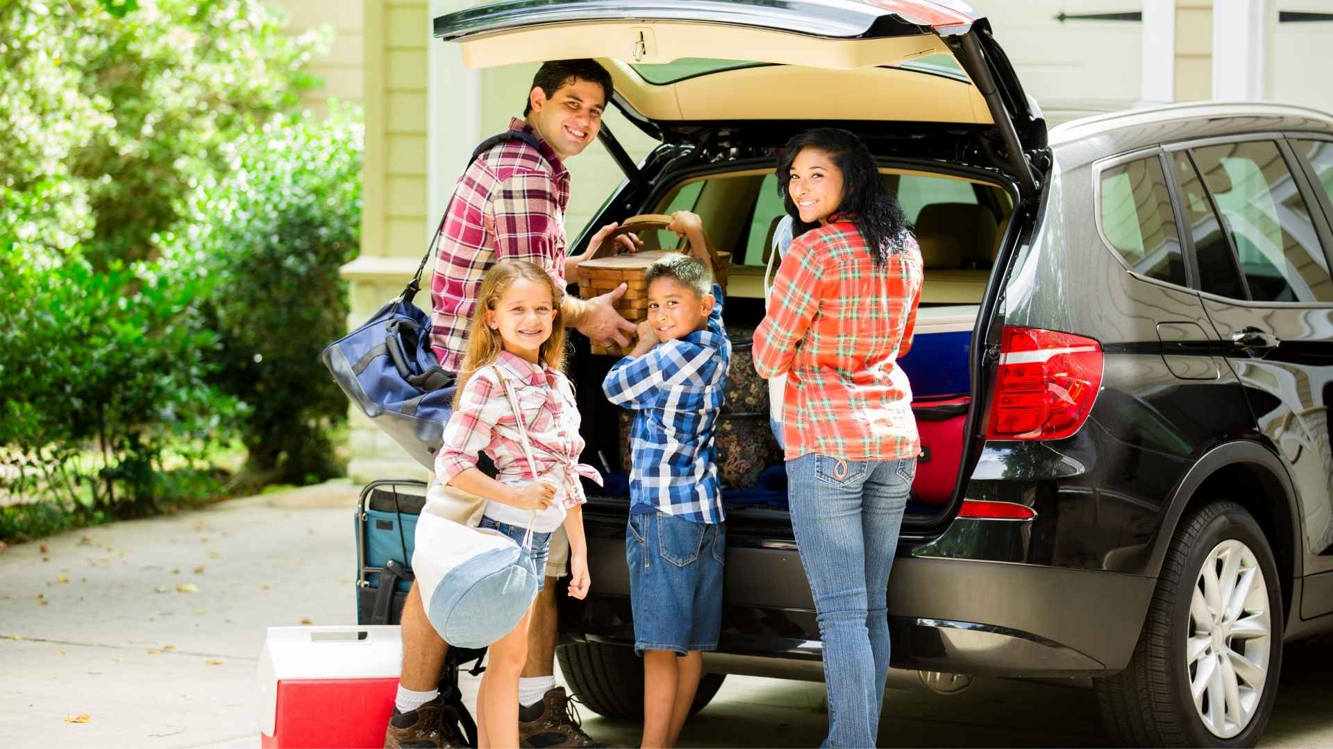 A family of four stands by an open SUV trunk
