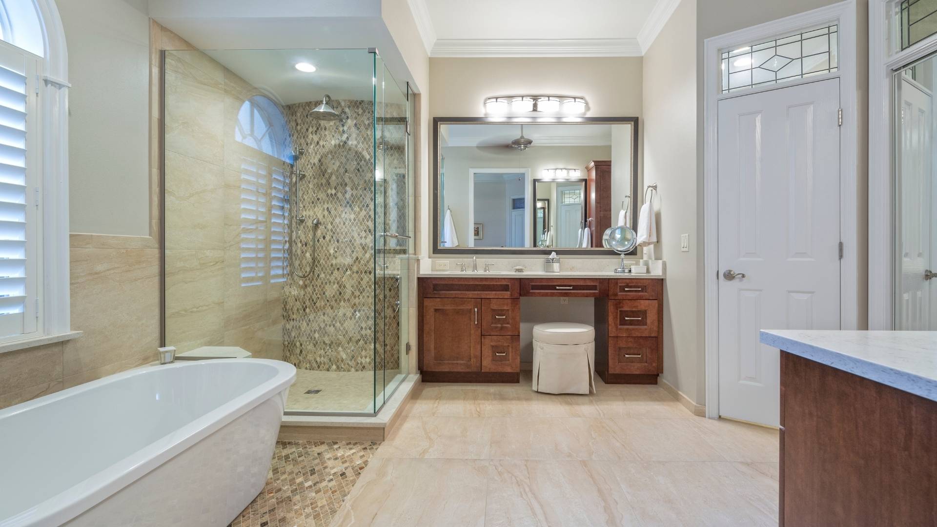 Modern bathroom with a freestanding bathtub, glass-enclosed shower, wooden vanity with mirror and lights, tiled floor, and neutral color palette—check your gas line for safety before enjoying this serene space.