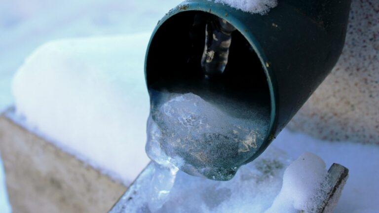 Close-up of a green metal pipe with ice partially blocking the opening.