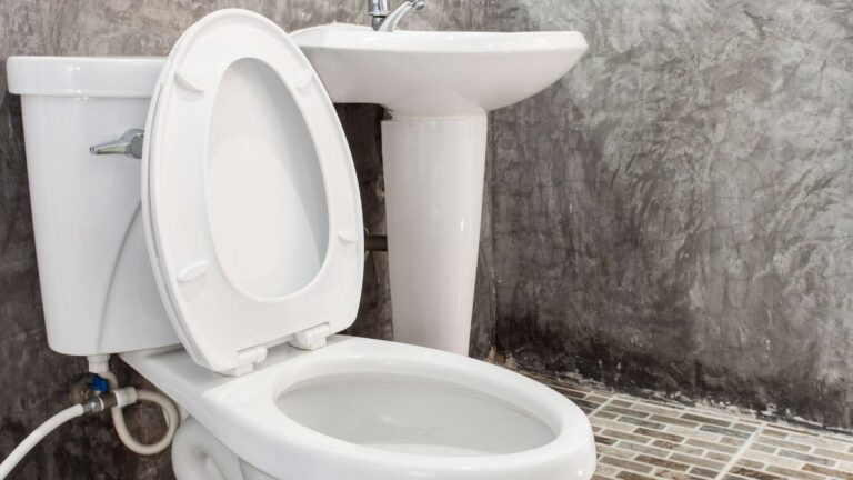 white toilet with led up next to a white sink in grey bathroom with tile flooring
