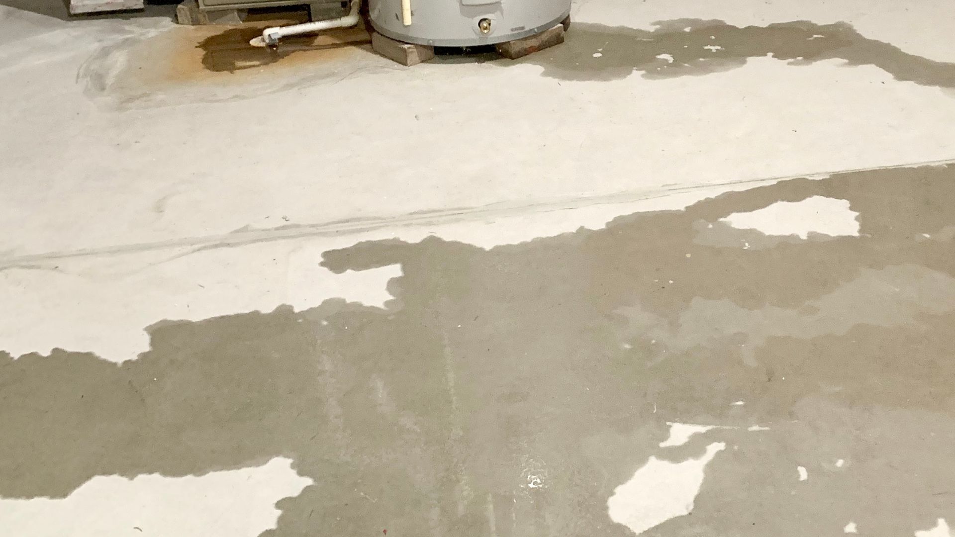 Water has pooled on a concrete basement floor near a water heater, indicating a leak.