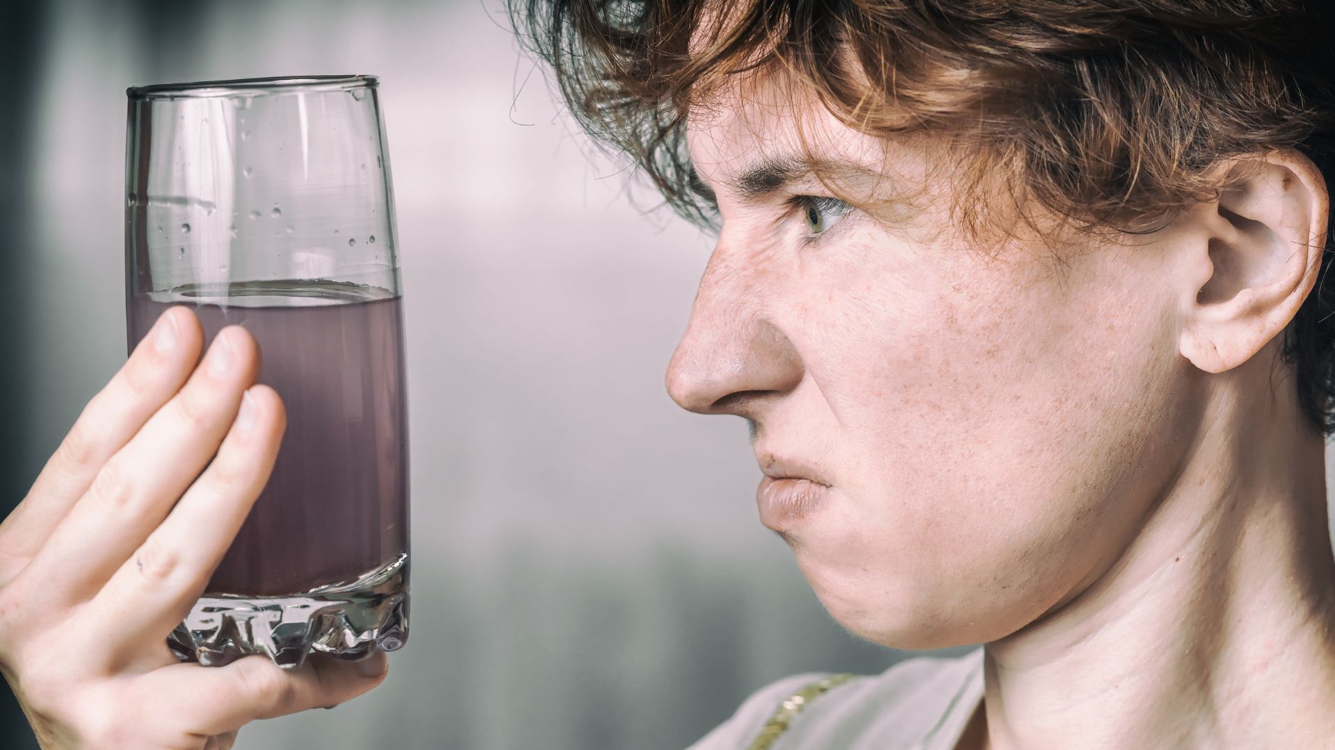 A woman looking skeptically at a glass of murky purple liquid.